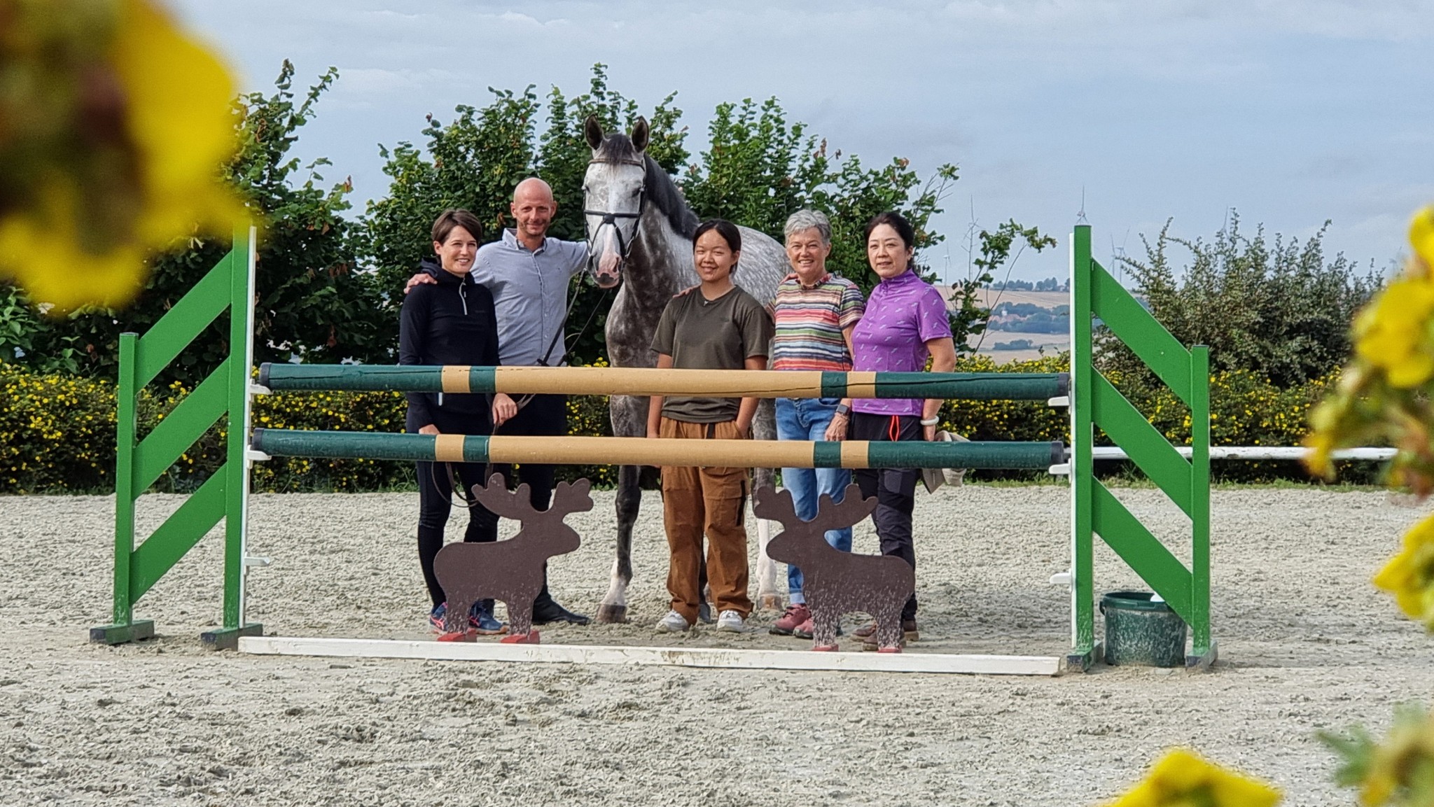 Gruppenfoto mit Schimmel vor einem Springhindernis auf dem Reitplatz